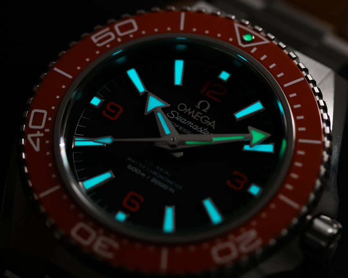 mega Planet Ocean 600M lume shot showing glowing markers on orange bezel model