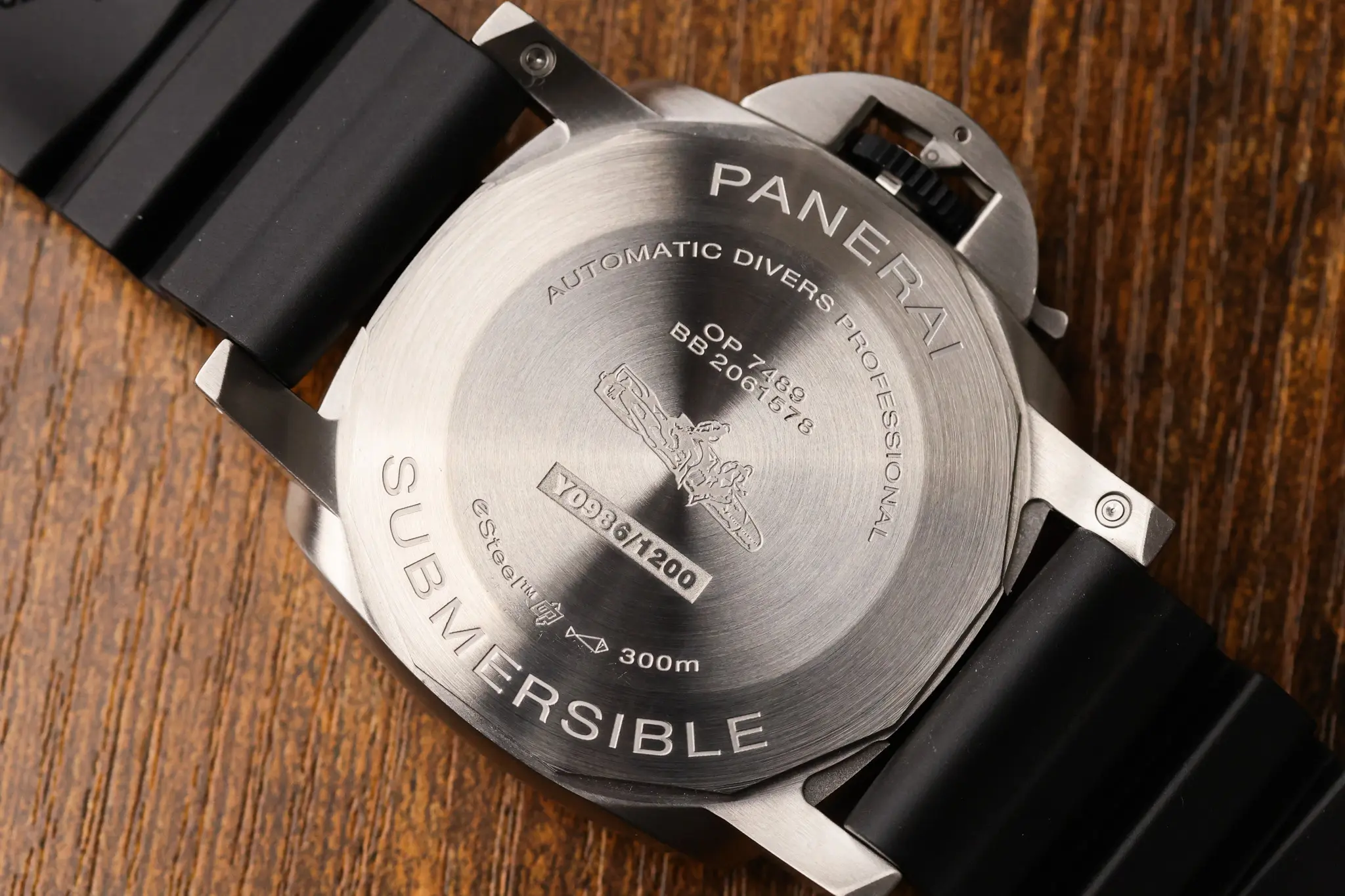 Caseback view of Panerai Submersible QuarantaQuattro Grigio Roccia PAM01288 on black strap against wood background
