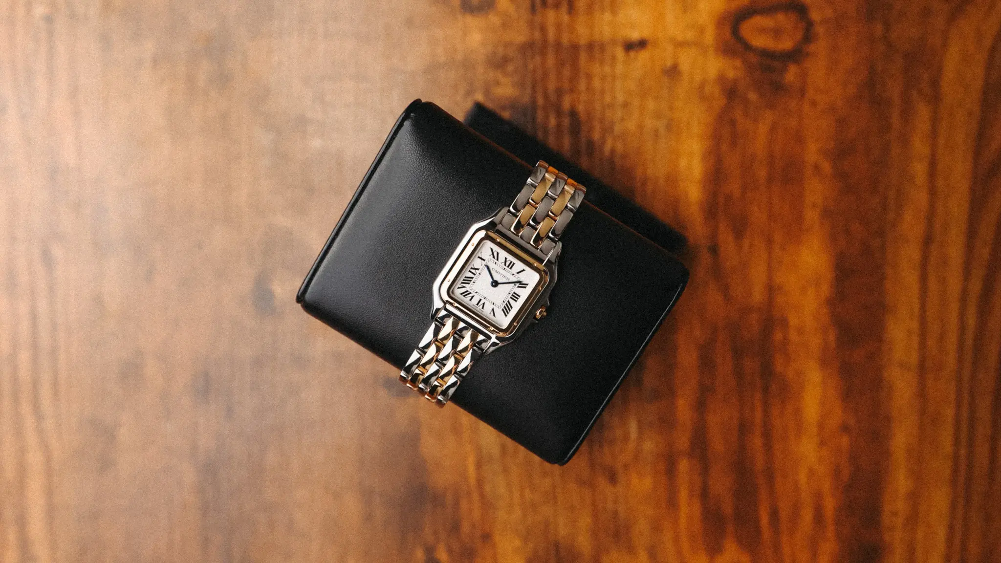 Cartier Panthère watch photographed from above on a black stand with warm wood background