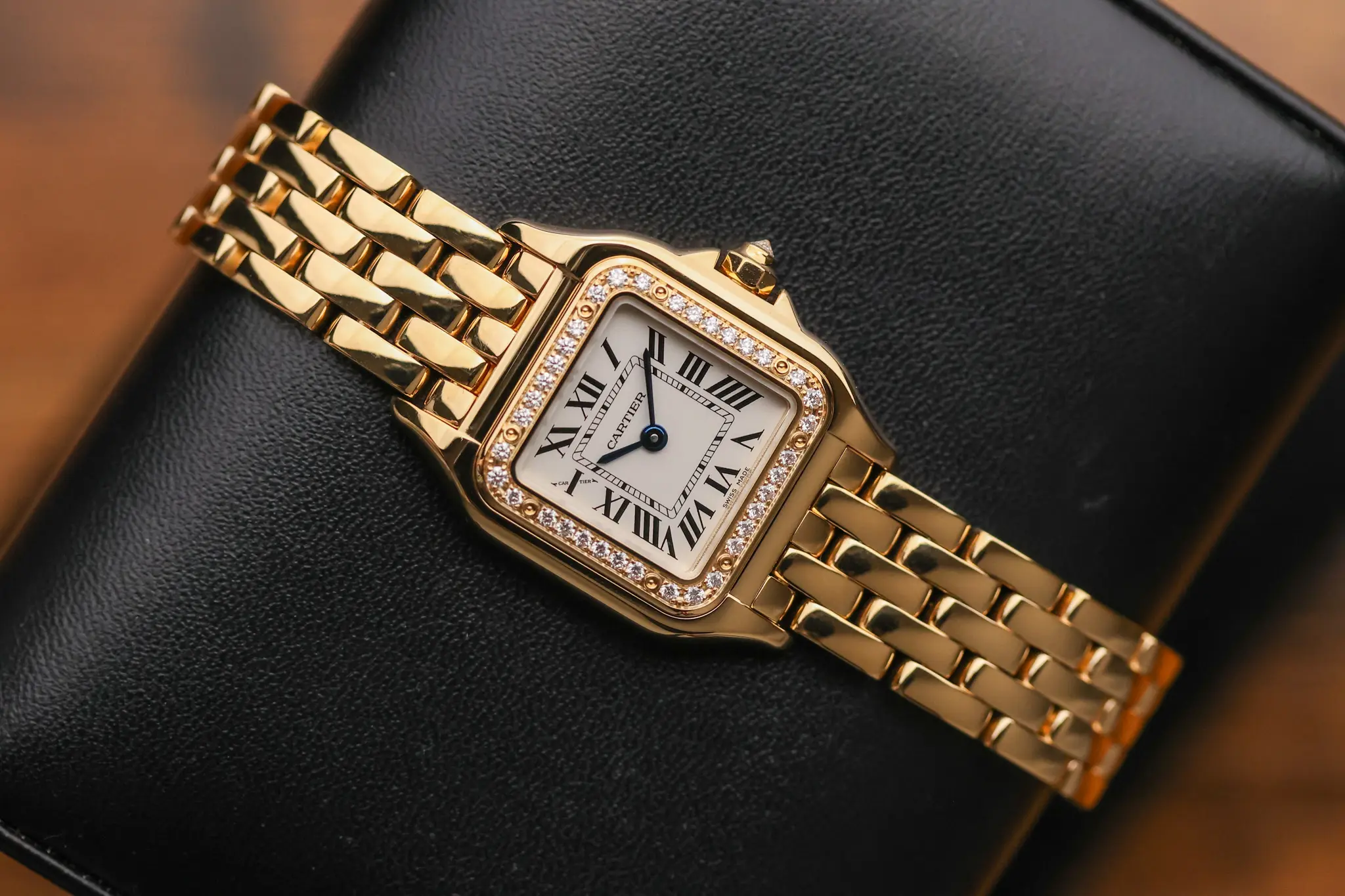 Front angled view of yellow gold Cartier Panthère watch with diamond-set bezel on black cushion