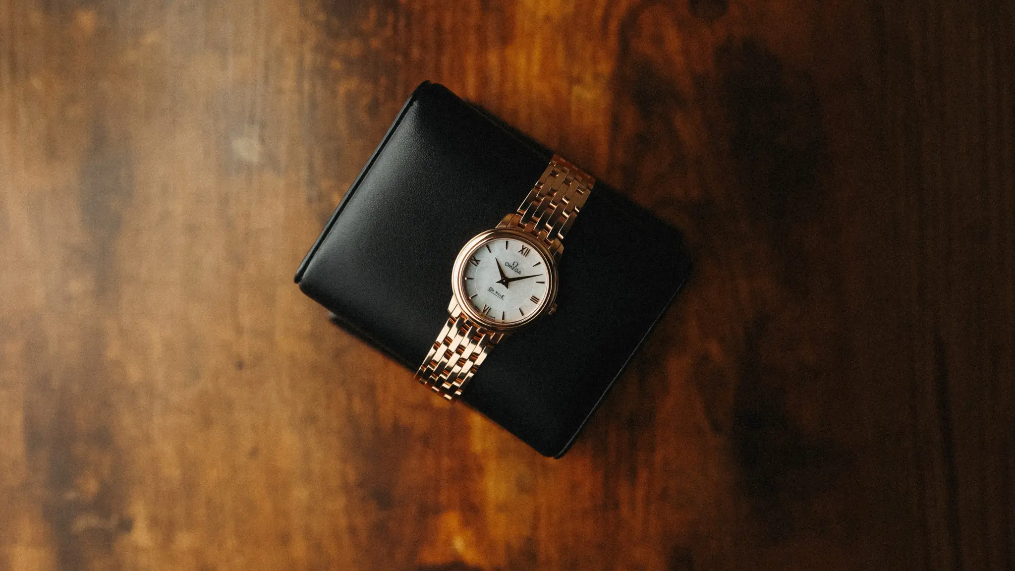 Omega De Ville Prestige rose gold bracelet watch with mother-of-pearl dial resting on leather cushion