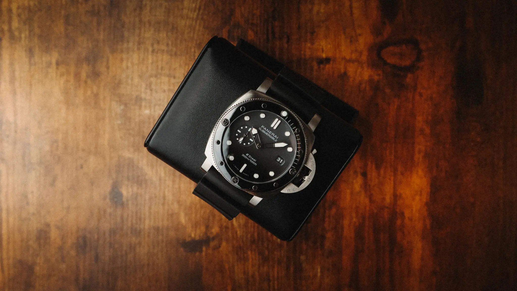 Panerai Submersible QuarantaQuattro Grigio Roccia PAM01288 photographed from above on a black stand with warm wood background