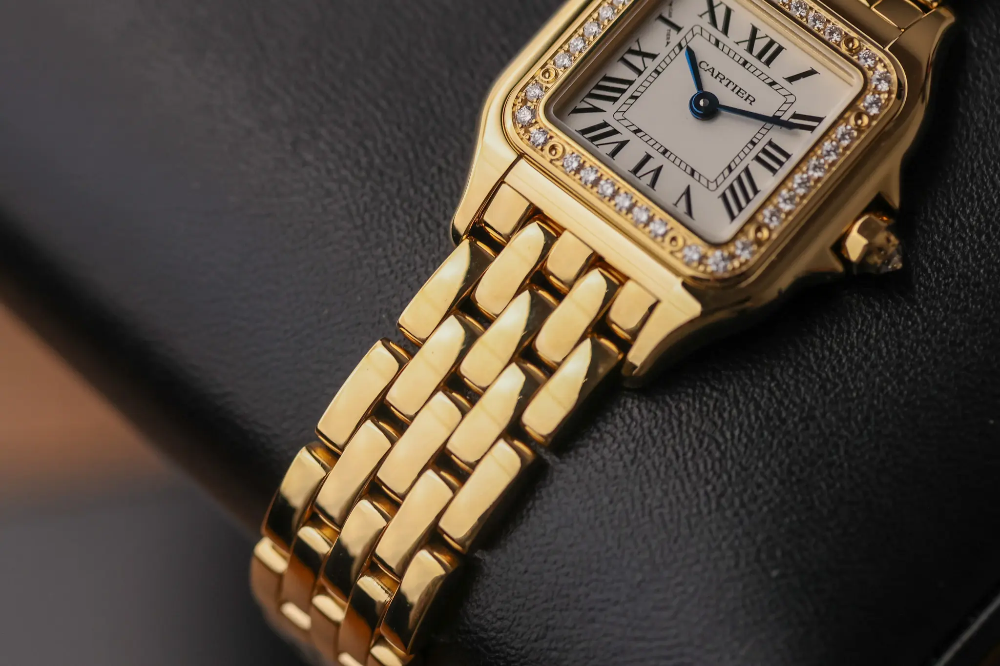 Yellow gold Cartier Panthère watch on black cushion showing bracelet design and diamond-set bezel